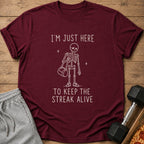Maroon t-shirt with white text and skeleton graphic saying "I'M JUST HERE TO KEEP THE STREAK ALIVE".