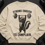 "Strong Enough To Complain" text over skunk lifting barbell graphic on tan sweatshirt.