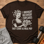 Brown t-shirt graphic of a woman holding cupcakes with text "I BROUGHT RECOVERY CUPCAKES THEY COUNT AS MEAL PREP".