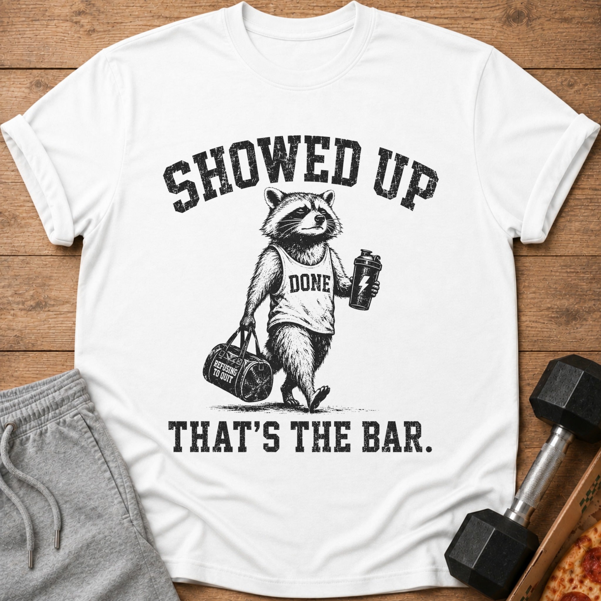 White t-shirt with a raccoon wearing a "DONE" tank top, holding a shaker and gym bag, with text.