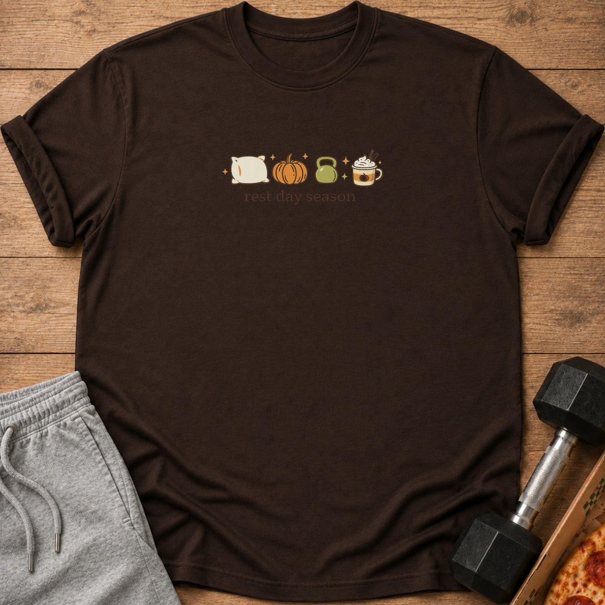 Brown t-shirt with pillow, pumpkin, kettlebell, and latte icons above text "rest day season".