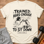 Cream t-shirt with "Trained Hard Enough To Sit Down" graphic.