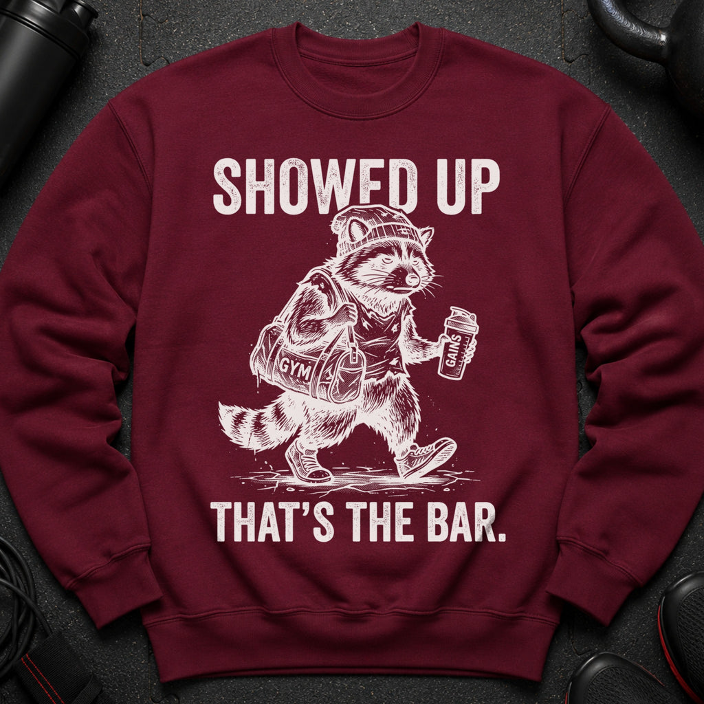 Maroon sweatshirt with graphic of a raccoon in gym clothes carrying a bag and shaker bottle.