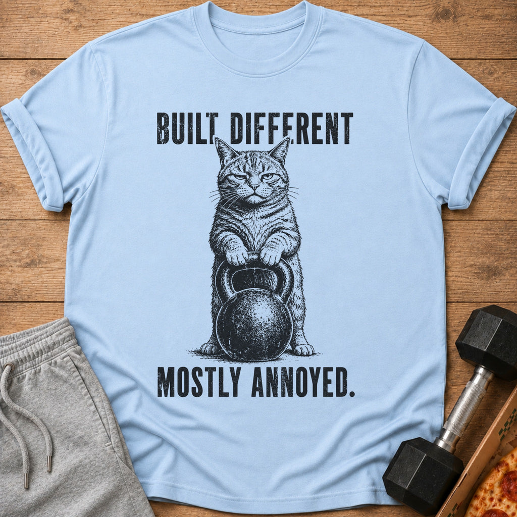 Light blue t-shirt with graphic of cat holding kettlebell, text says "BUILT DIFFERENT MOSTLY ANNOYED."
