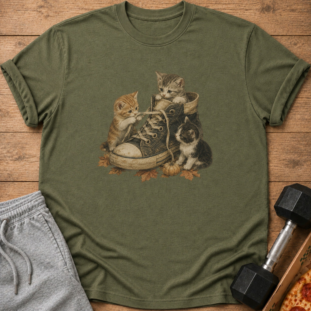 Three kittens play with shoelaces inside a worn sneaker among autumn leaves.