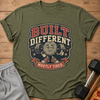 Green t-shirt with graphic of cartoon dumbbell character saying "BUILT DIFFERENT MOSTLY TIRED."