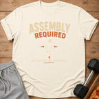 Cream t-shirt with "ASSEMBLY REQUIRED MOTIVATION SOLD SEPARATELY" text.