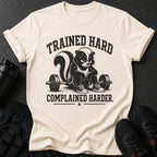 Trained hard complained harder graphic on a cream t-shirt with a skunk at a barbell.