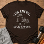 Brown t-shirt with white text and graphics of a kettlebell, dumbbell, and battery.