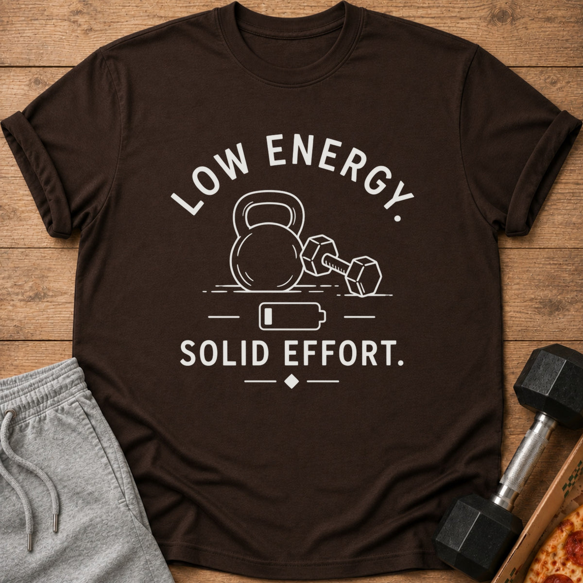 Brown t-shirt with white text and graphics of a kettlebell, dumbbell, and battery.