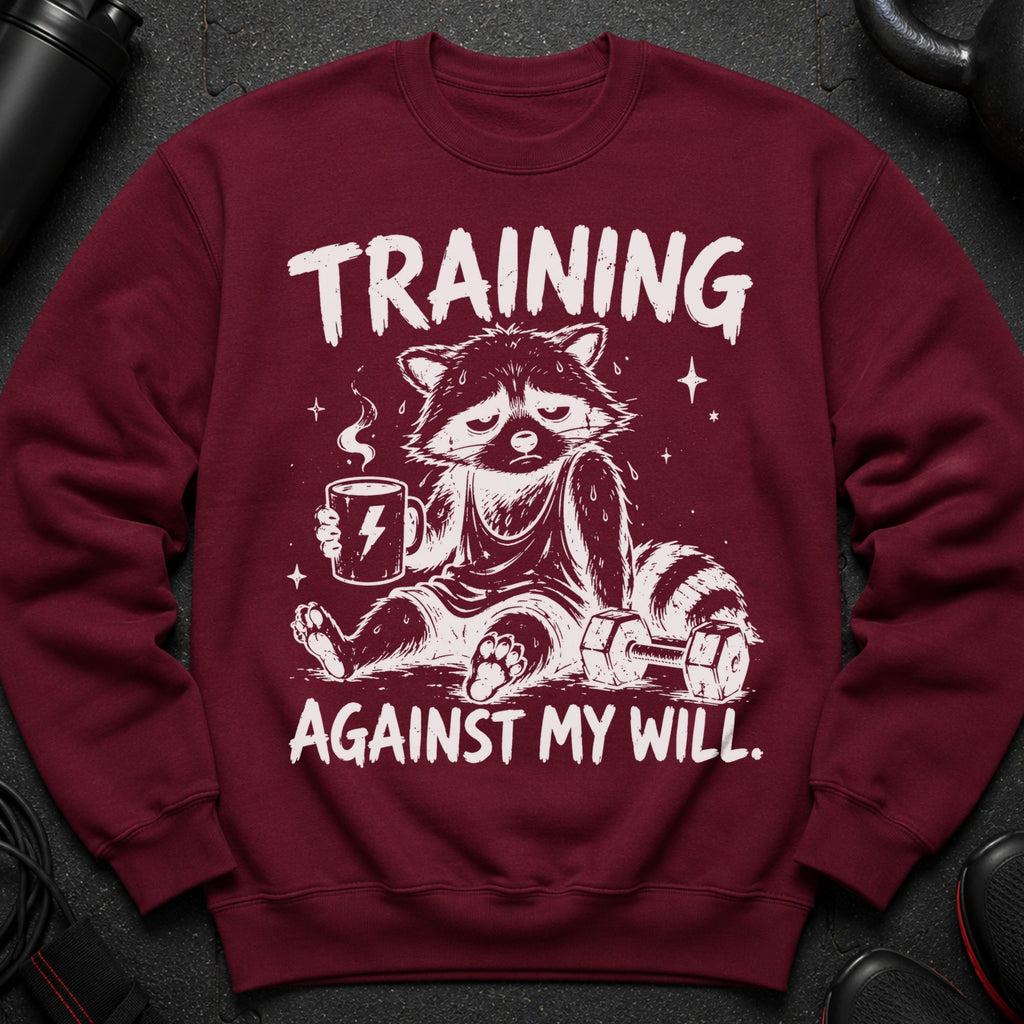 Maroon sweatshirt with a tired raccoon holding coffee and a dumbbell, text reads "TRAINING AGAINST MY WILL."