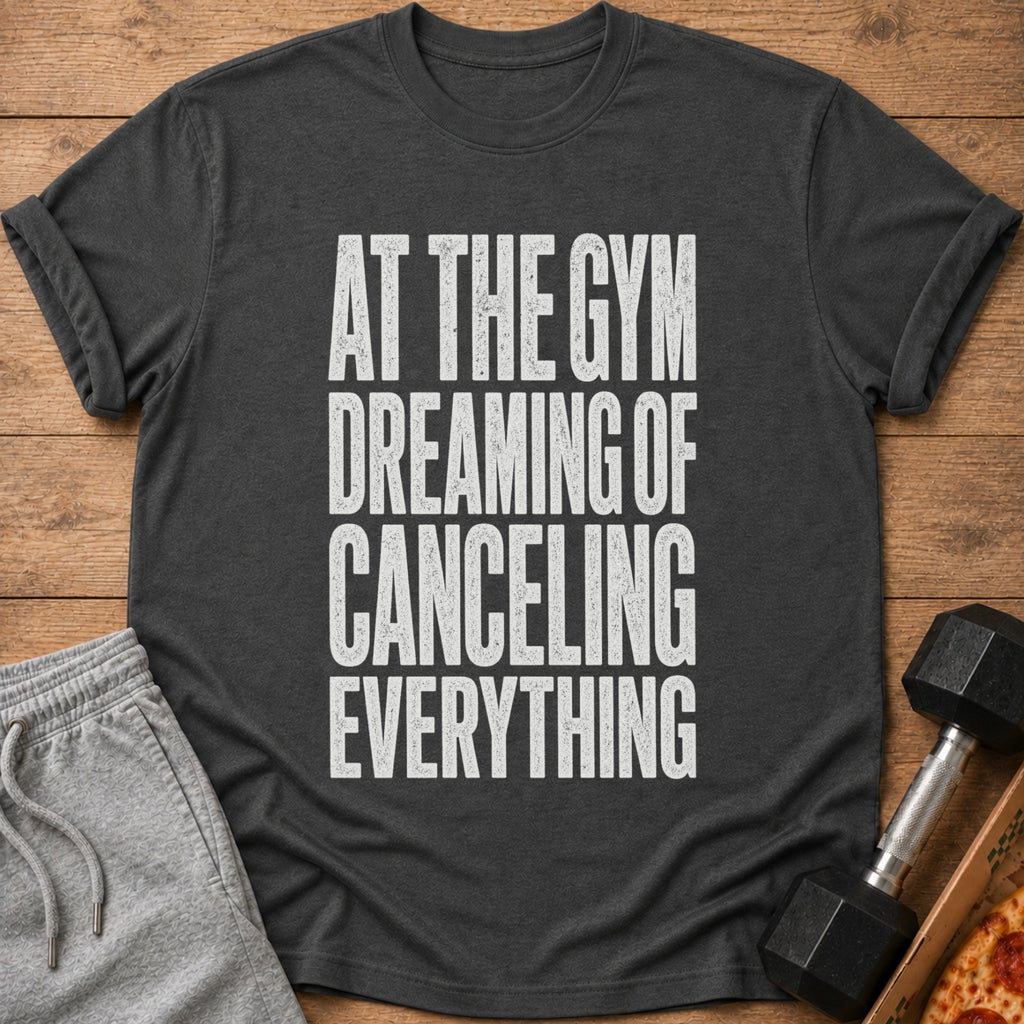 Dark gray t-shirt with white text: "AT THE GYM DREAMING OF CANCELING EVERYTHING".