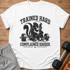 White t-shirt with a skunk lifting weights and text "TRAINED HARD COMPLAINED HARDER."