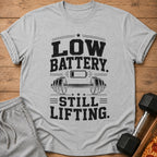 Grey t-shirt with "Low Battery. Still Lifting." text and a barbell graphic.