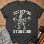 Dark grey t-shirt with skeleton lifting weights and text "NOT STRONG JUST STUBBORN".