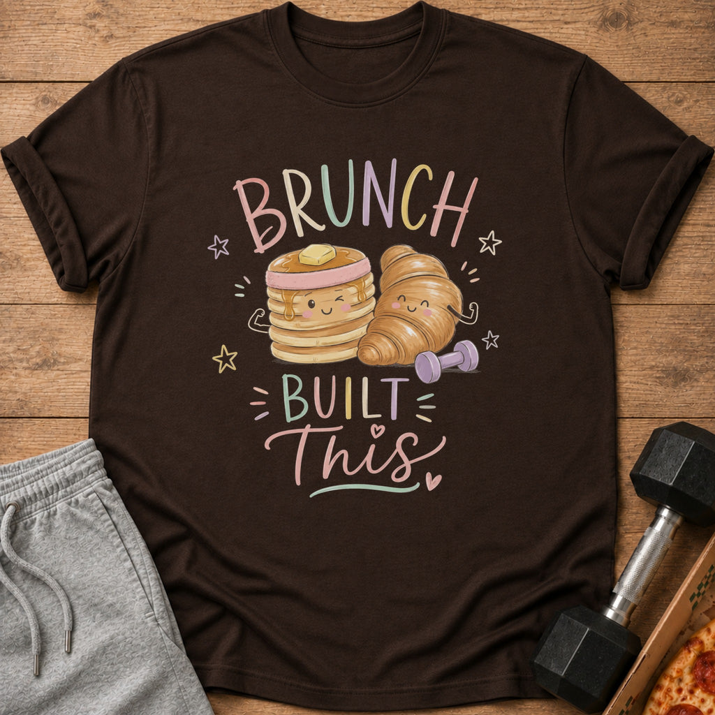 A brown crewneck t-shirt featuring a cartoon illustration of pancakes and a croissant flexing with dumbbells, with the text "BRUNCH BUILT THIS".