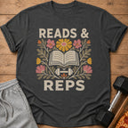 Dark gray t-shirt featuring a retro graphic with an open book, dumbbells, flowers, and the text READS & REPS.