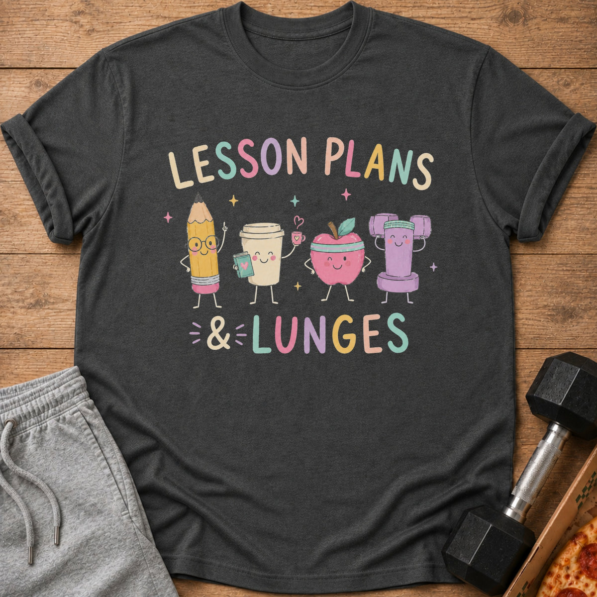 Dark gray t-shirt with cartoon pencil, coffee cup, apple, and dumbbell saying "Lesson Plans & Lunges".