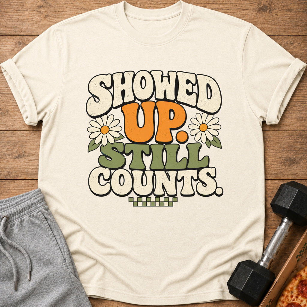 Cream t-shirt with "SHOWED UP. STILL COUNTS." in retro font and daisy graphics.