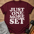 Maroon t-shirt with white text "JUST ONE MORE SET" and workout accessories.