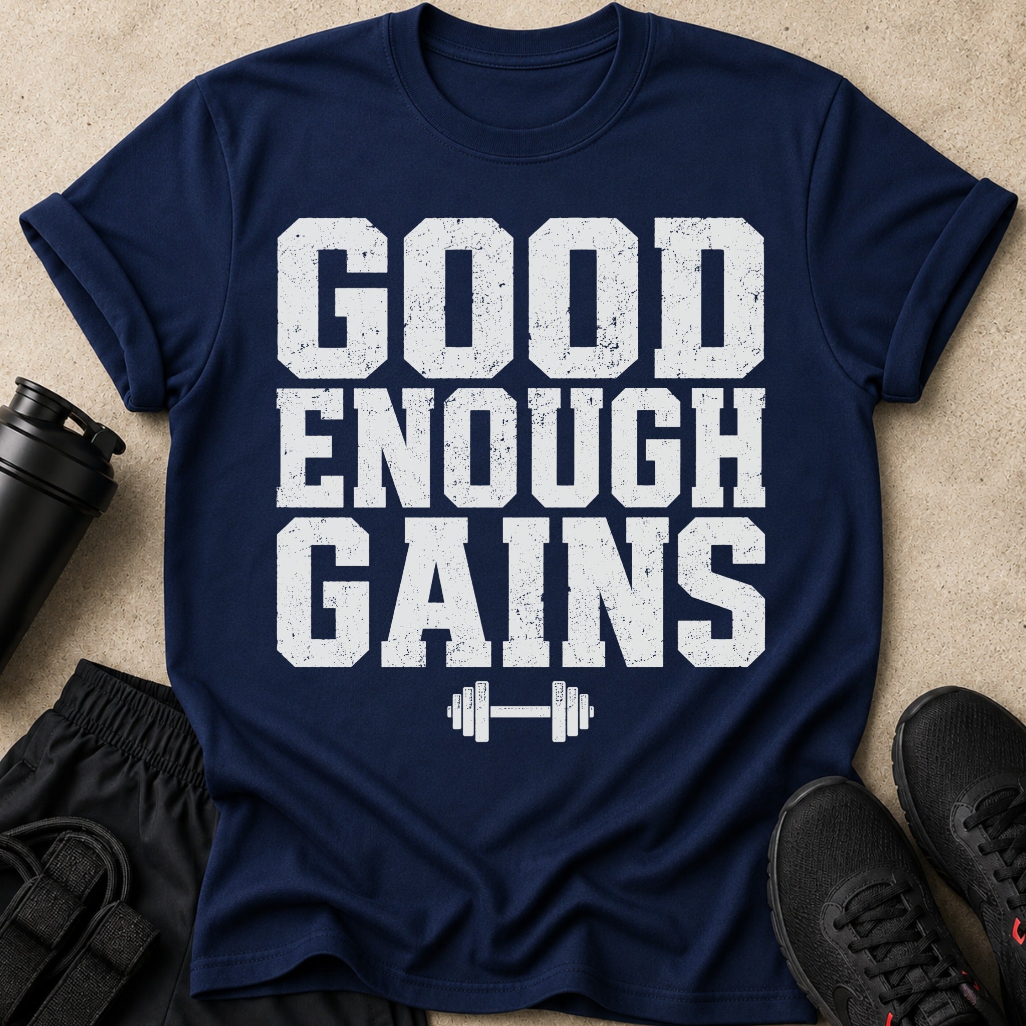 Navy t-shirt with distressed white text "GOOD ENOUGH GAINS" and a dumbbell graphic.