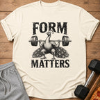 Off-white t-shirt featuring a black graphic of a peacock lifting a barbell, with text reading Form Matters.