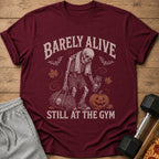 Maroon t-shirt with skeleton, gym bag, pumpkin, and text "Barely Alive Still at the Gym".