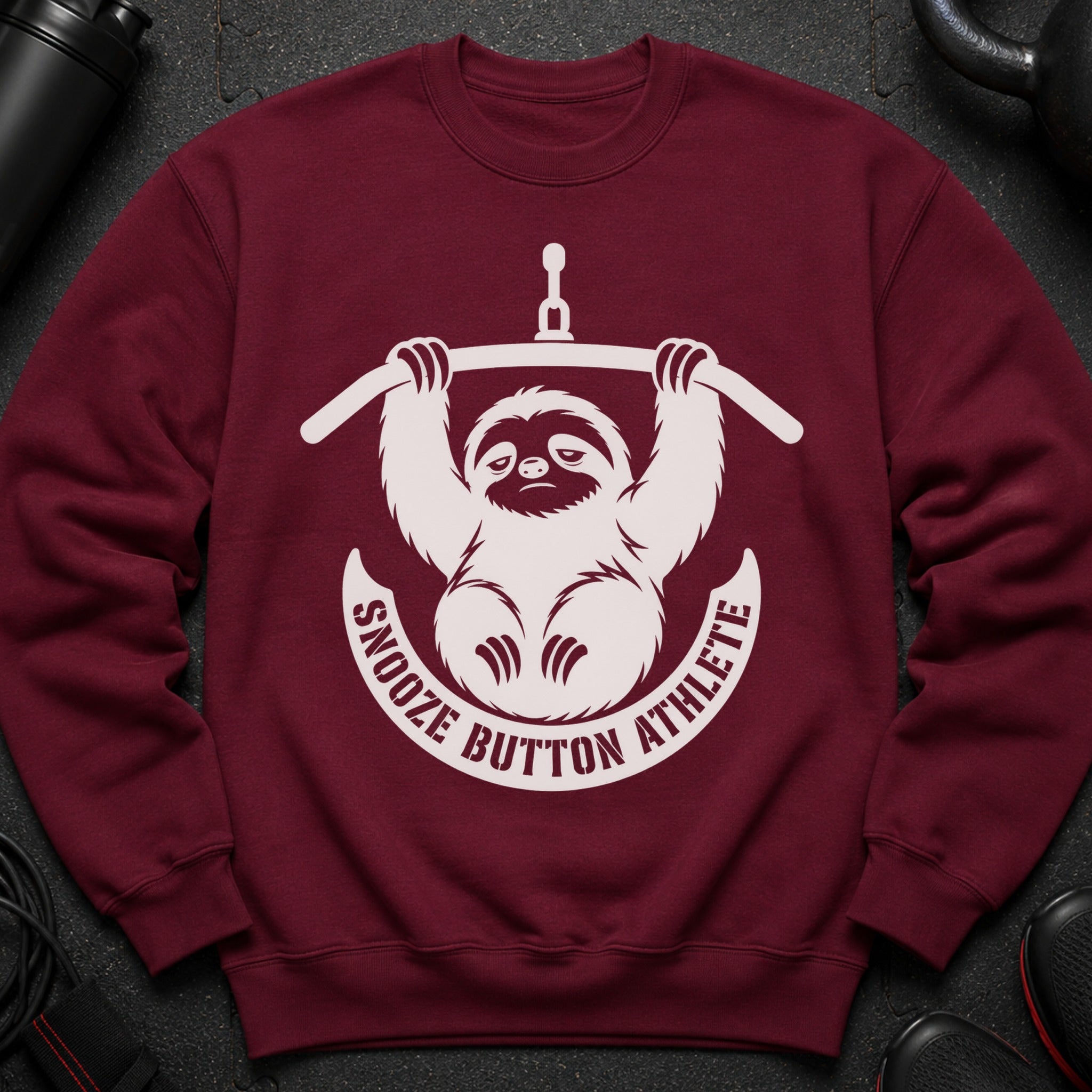 Maroon sweatshirt with white "Snooze Button Athlete" text circling a tired sloth holding a bar.