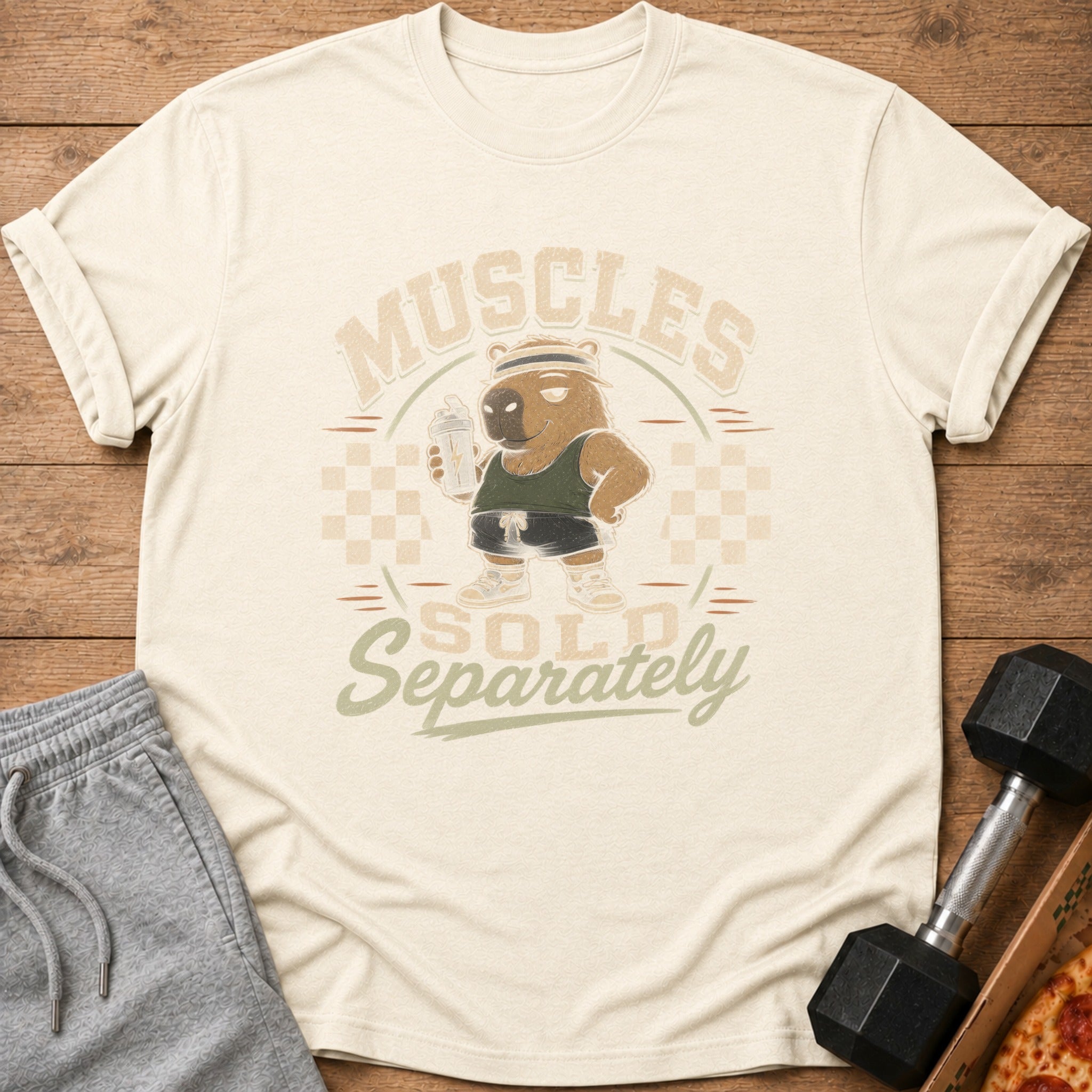Cream t-shirt with graphic of a capybara holding a shaker bottle, text reads "Muscles Sold Separately".