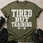 Green t-shirt with distressed white text "TIRED BUT TRAINING" and a barbell graphic.