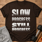 Brown t-shirt with distressed white text: "SLOW PROGRESS STILL PROGRESS".