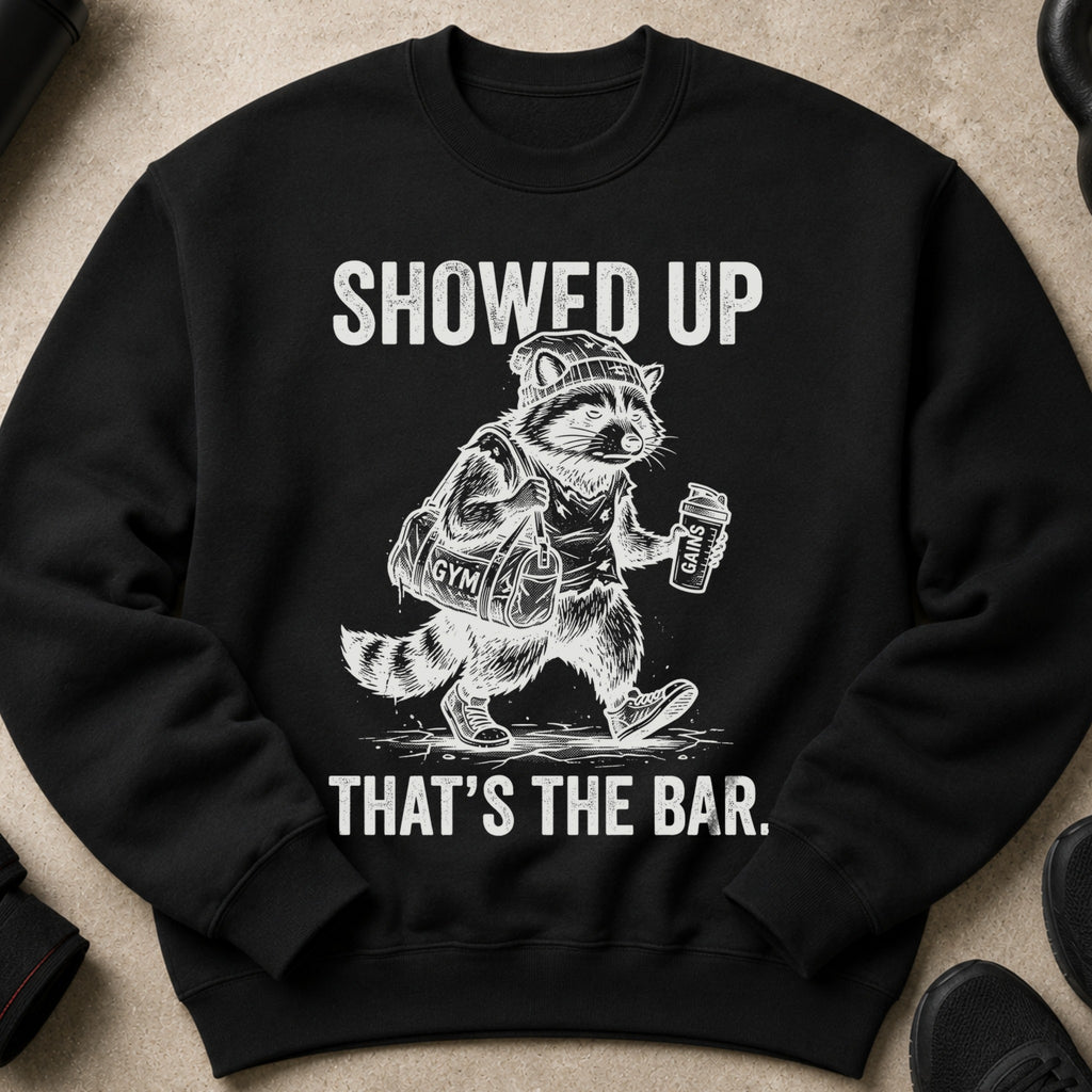 Black crewneck sweatshirt with a graphic of a raccoon in gym attire holding a gym bag and protein shake.