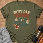 Olive green t-shirt with a cartoon couch giving a thumbs up and holding a drink, with "REST DAY LEGEND" text.
