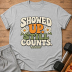 Grey t-shirt with "SHOWED UP. STILL COUNTS." text and daisy graphics.