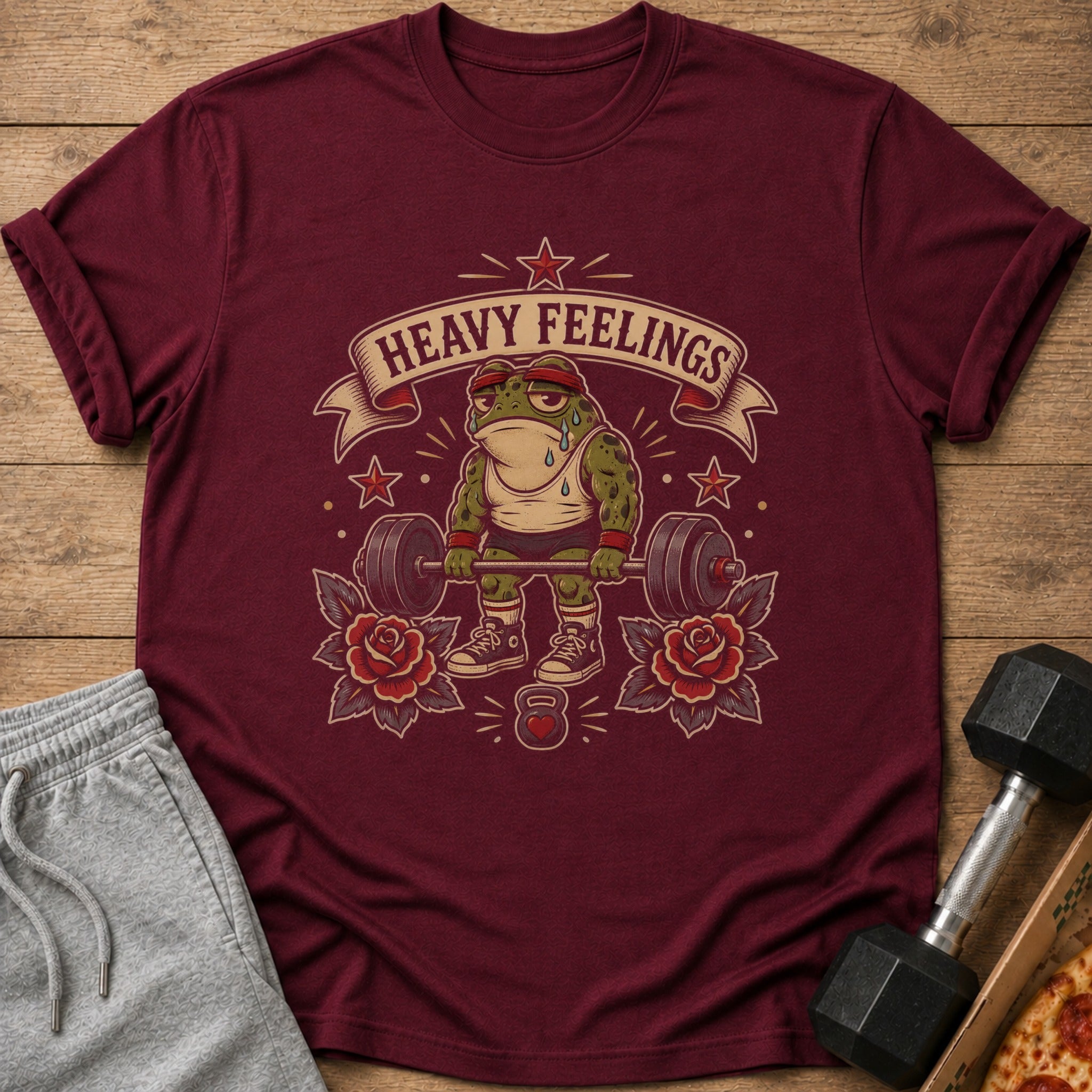 Maroon t-shirt featuring a cartoon frog lifting weights with the text "HEAVY FEELINGS".