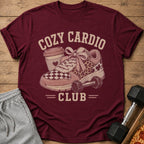 Maroon t-shirt with "Cozy Cardio Club" graphic featuring a sneaker, coffee cup, and dumbbell.