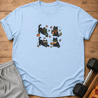 Light blue t-shirt with four cartoon black cats and fall leaves.