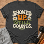 Dark t-shirt with retro graphic "SHOWED UP. STILL COUNTS." and daisies.