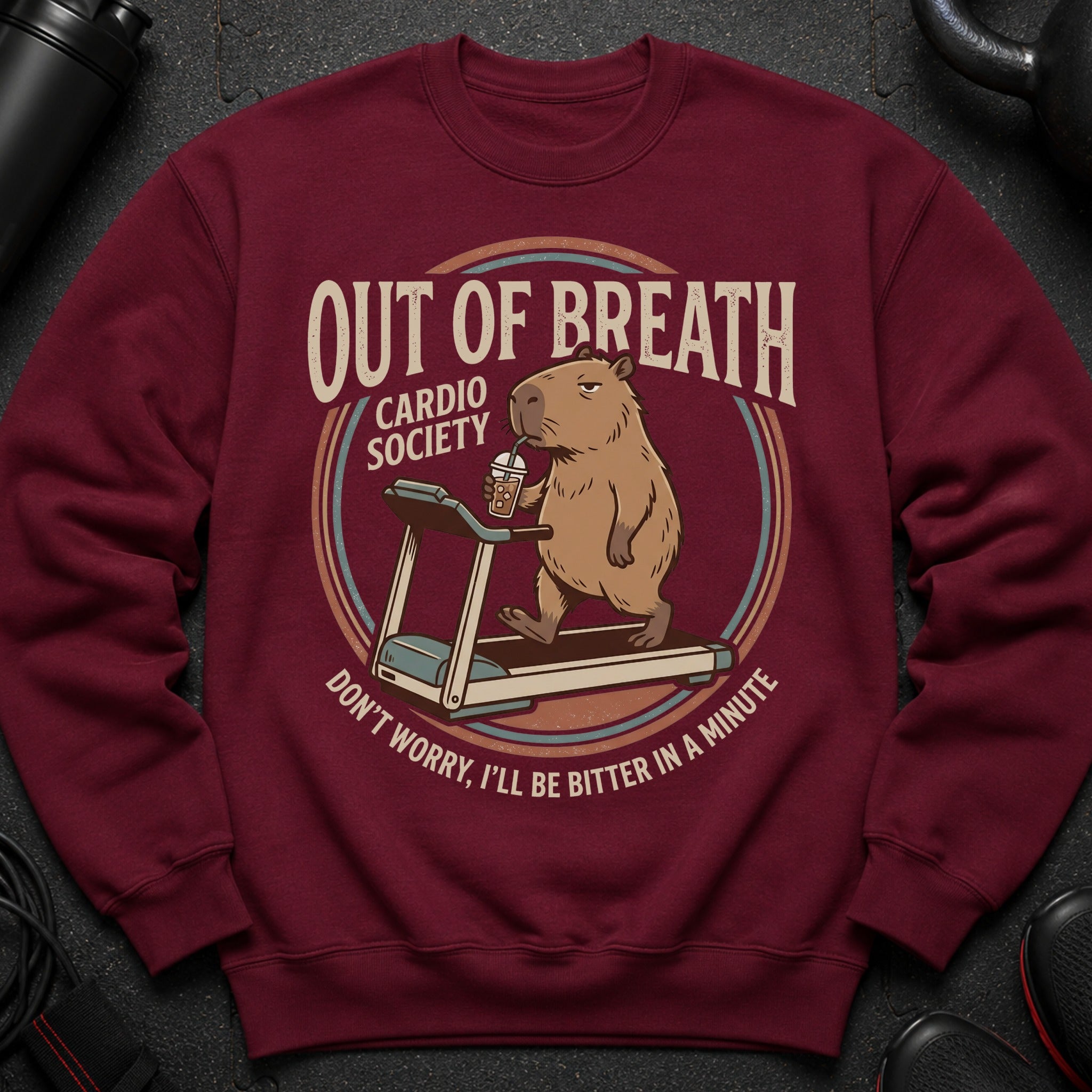 Maroon sweatshirt with a graphic of a capybara on a treadmill drinking coffee.