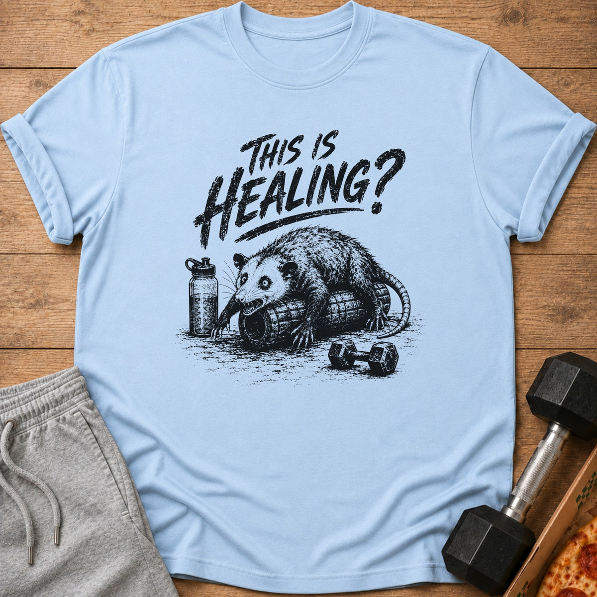 Light blue t-shirt graphic of a possum on a foam roller with text "This is Healing?".