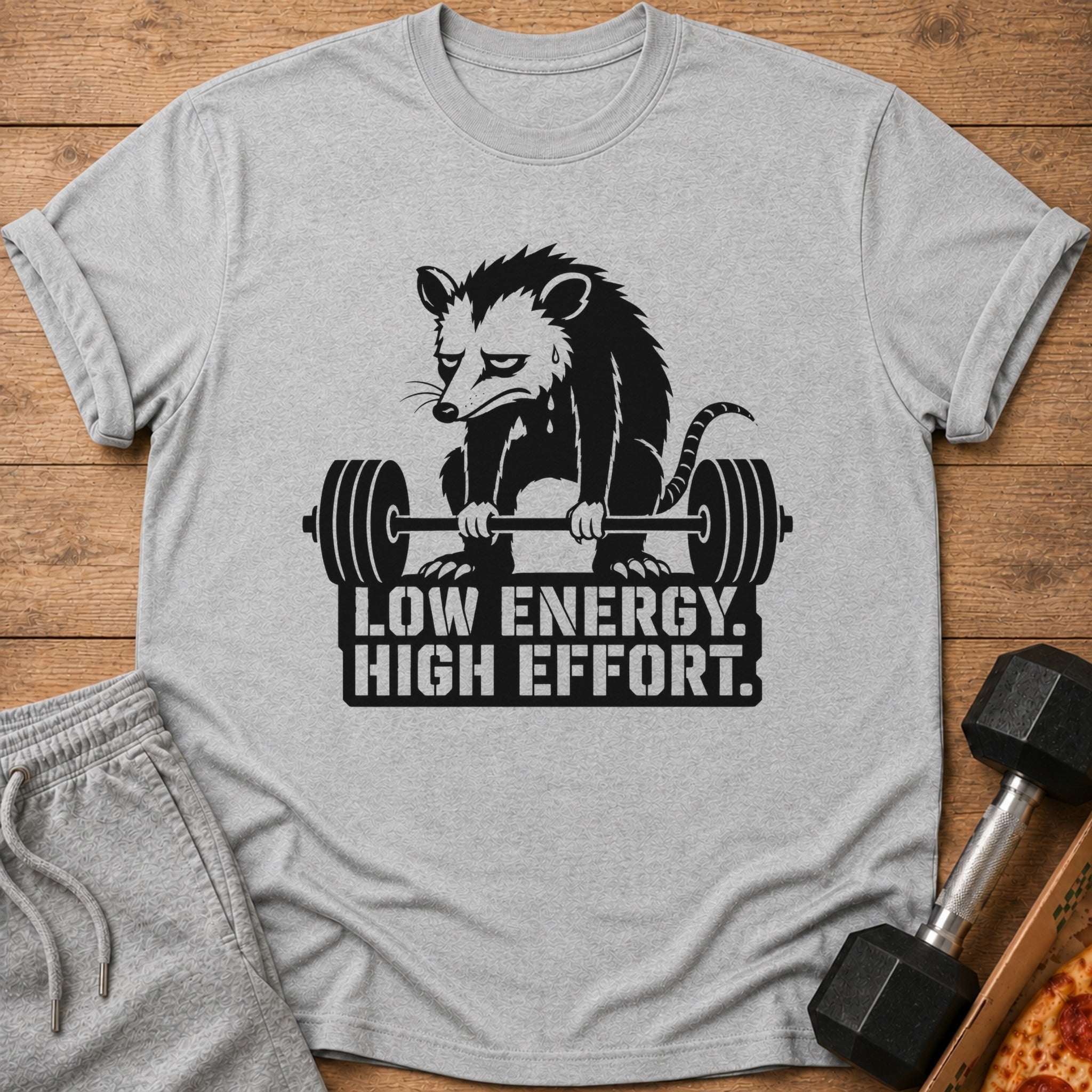 T-shirt graphic featuring a sad possum lifting a barbell with text "LOW ENERGY. HIGH EFFORT."