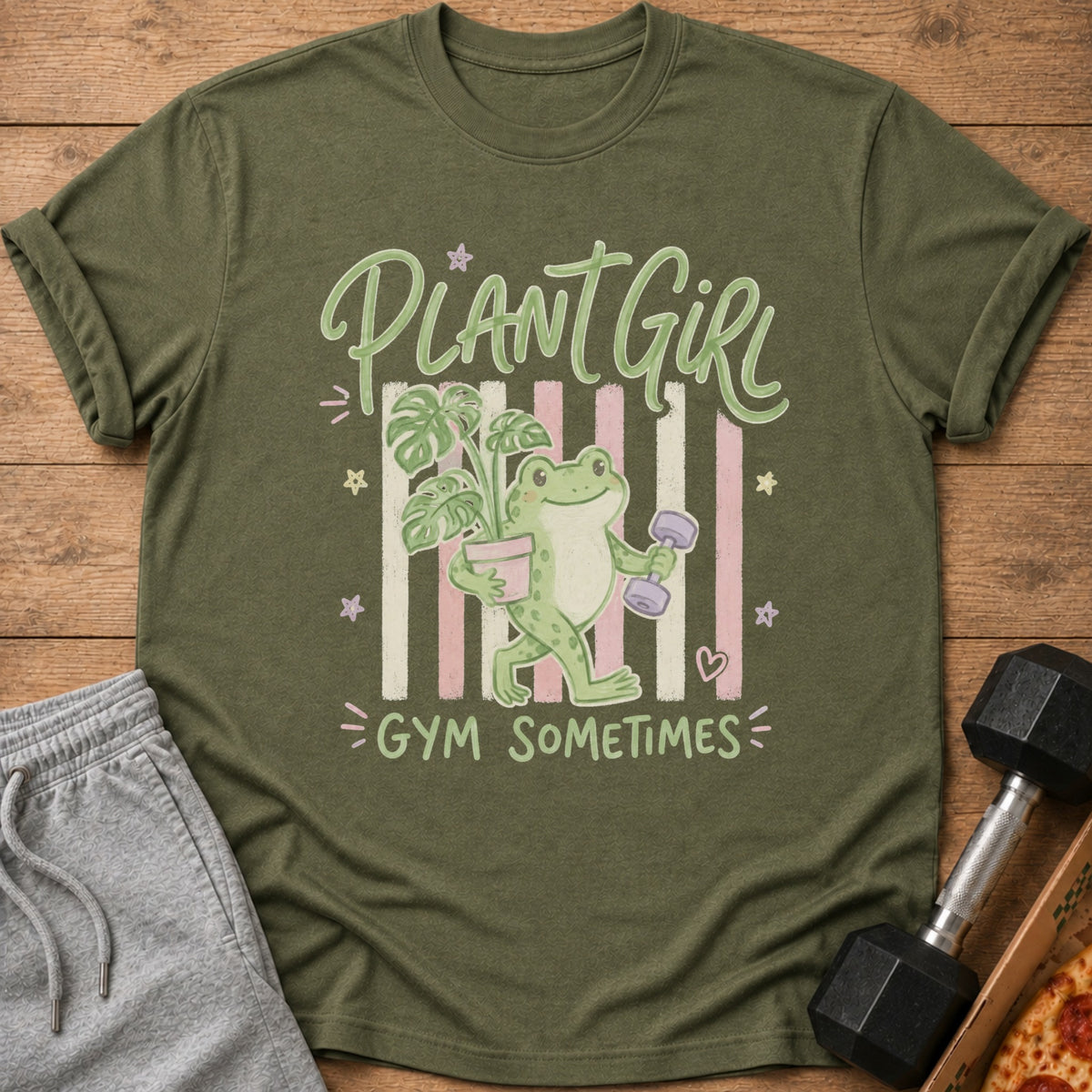 Green t-shirt with cartoon frog holding plant and dumbbell, text reads "PLANT GIRL GYM SOMETIMES."