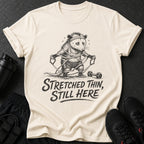 Cream t-shirt with opossum workout graphic and "Stretched Thin, Still Here" text.
