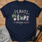 Navy t-shirt with "PLANTS & PERSONAL BESTS" and cute plant, cactus, watering can, shoe, and dumbbell characters.