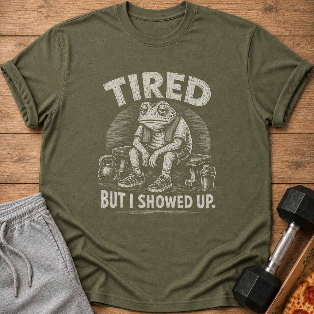 Olive green t-shirt with a tired frog illustration and the text "TIRED BUT I SHOWED UP."