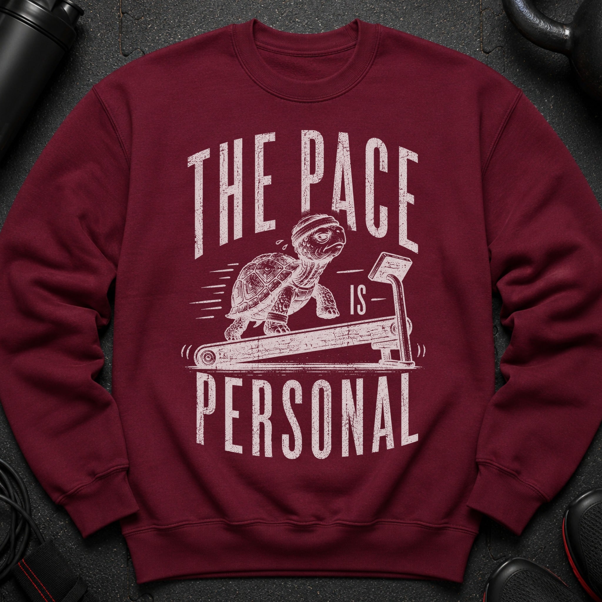 Maroon sweatshirt with distressed graphic of a turtle on a treadmill and text "THE PACE IS PERSONAL".