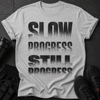 Gray t-shirt with "SLOW PROGRESS STILL PROGRESS" text in distressed black font.
