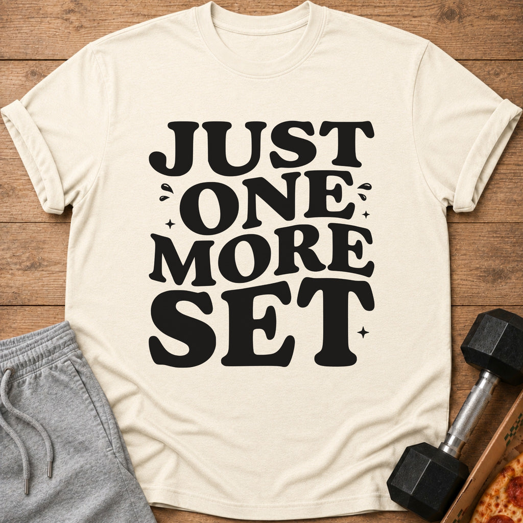 Cream t-shirt with "JUST ONE MORE SET" in black text, next to workout shorts and dumbbell.