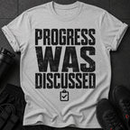 Grey t-shirt with black distressed text "PROGRESS WAS DISCUSSED" and a clipboard icon.