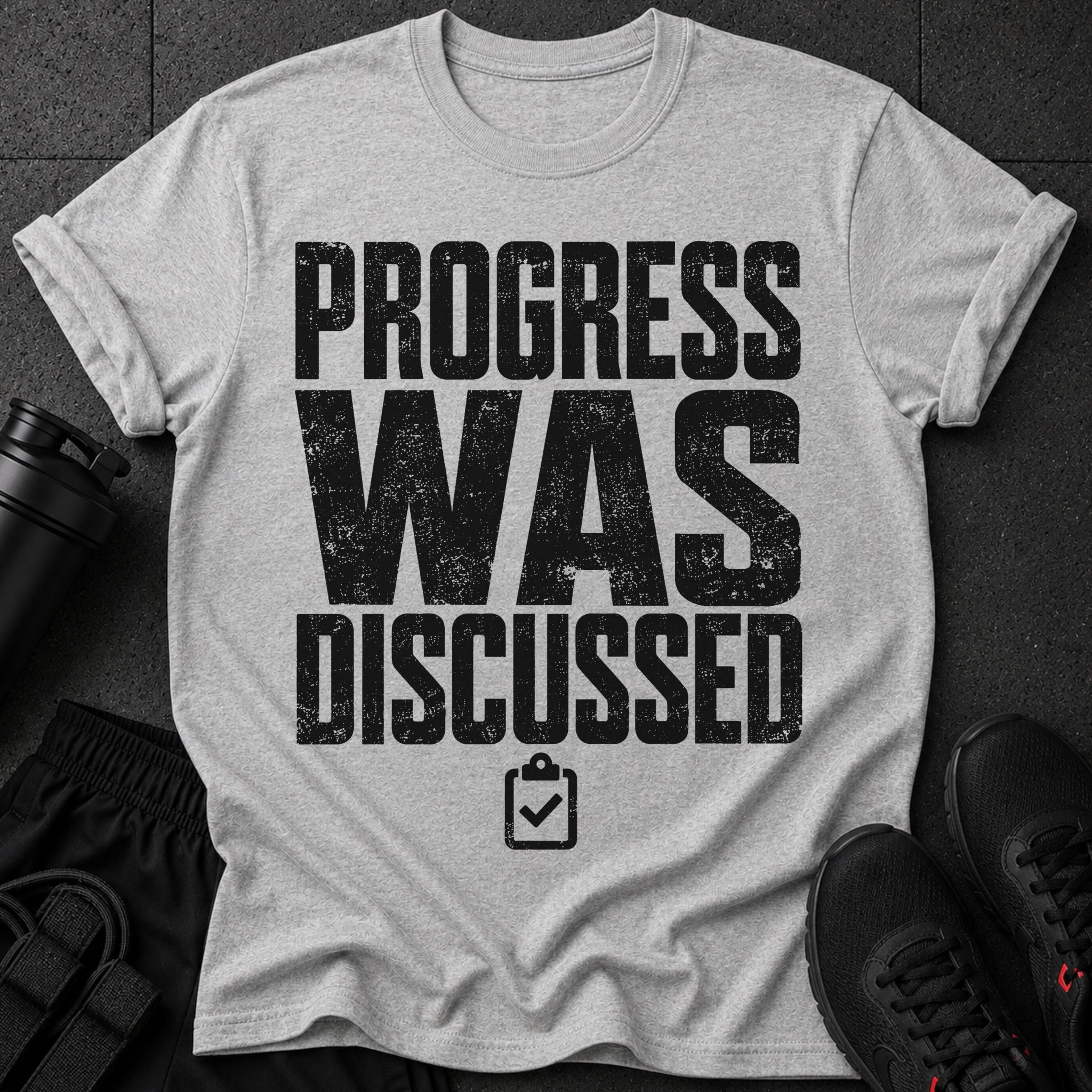 Grey t-shirt with black distressed text "PROGRESS WAS DISCUSSED" and a clipboard icon.